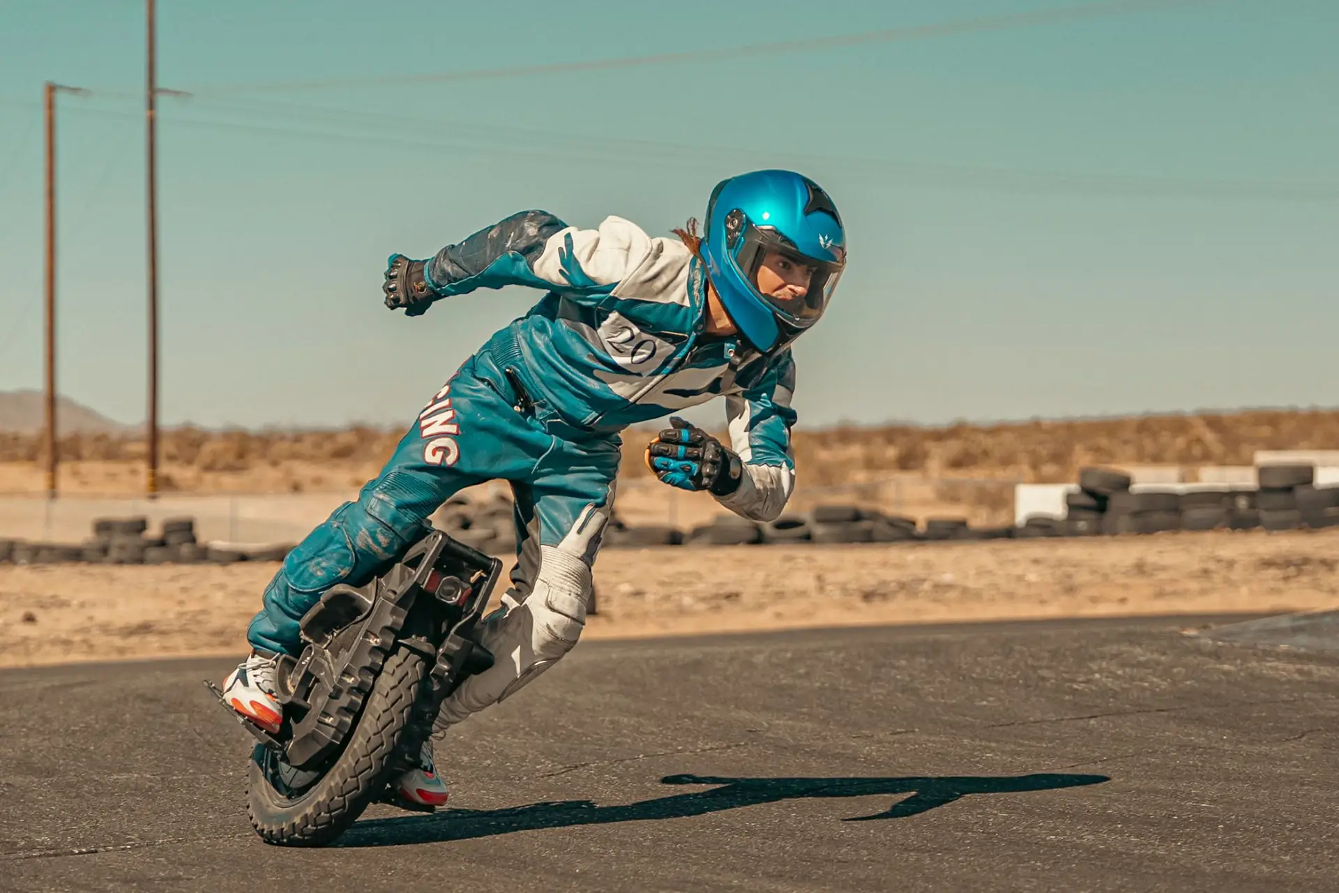 A rider in full protective gear leaning an electric unicycle into a corner on a closed track